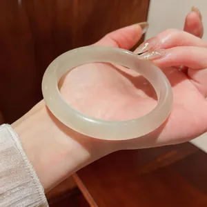 Primer plano de un brazalete de piedra de ojo de gato blanco translúcido en la muñeca.