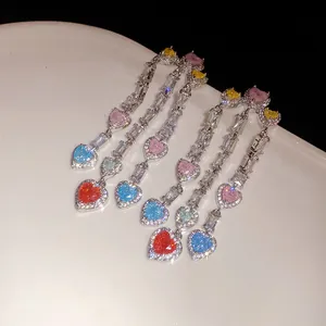 Close-up of elegant long tassel earrings with colorful heart zircons on a white plate