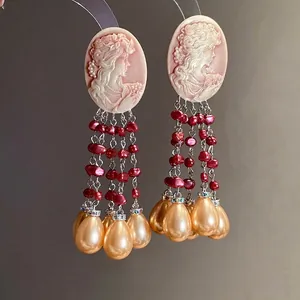 Elegant vintage cameo earrings featuring red and champagne pearl tassels on grey background