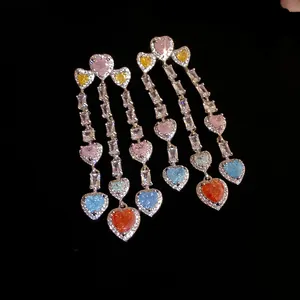 Close-up of heart-shaped multi-color zircon tassel earrings on black background.