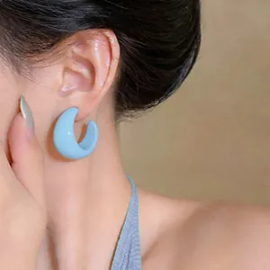 Detailed close-up showing a light blue C-shaped resin stud earring worn by a model
