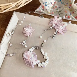 Elegantes Schmuckset mit rosa Chiffonblumen und Perlen: Halskette, Armband und Ohrringe.