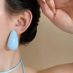 Detailed close-up of large light blue teardrop resin earrings worn by Asian model
