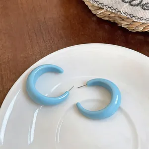 Close-up of candy-colored light blue C-shaped resin hoop earrings on a white plate
