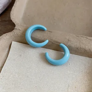 Close-up of bright sky blue C-shaped resin hoop earrings on a beige background