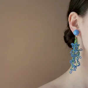 Close-up of blue beaded flower dangling earring worn by a model for beach vacation style