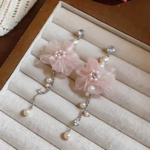 Nahaufnahme von rosa Chiffon-Blumen-Ohrhängern mit Perlen und Kristallen auf einem Tablett.