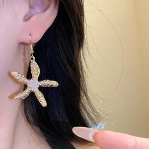 Detailansicht eines goldenen Seestern-Ohrrings mit Perlenverzierung an einem Modell