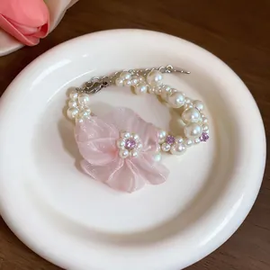 Nahaufnahme eines zarten Armbands mit rosa Chiffonblumen und eleganten weißen Perlen.
