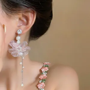 Detailansicht eines eleganten Ohrrings mit rosa Chiffonblume und Perlen an Model