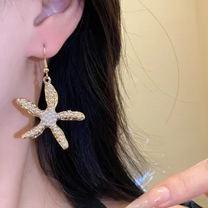 Detailaufnahme eines eleganten goldenen Seestern-Ohrrings mit weißen Perlen verziert