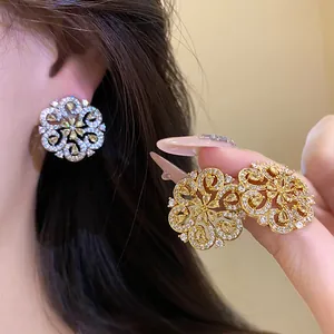 Close-up of gold and silver hollow floral stud earrings featuring intricate pavé yellow crystals.