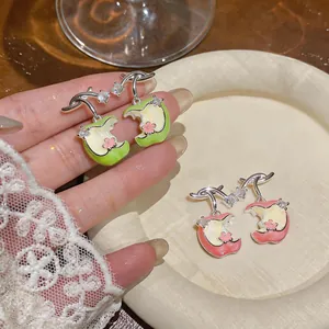 Vista detallada de los pendientes de manzana en esmalte y circón con toques florales.