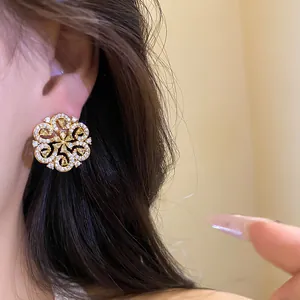 Close-up view of elegant hollow flower stud earrings with yellow and white stones.