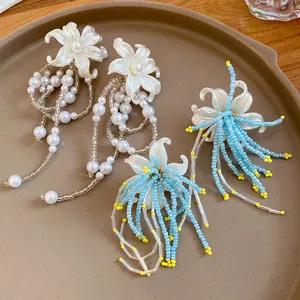 Close-up detail of elegant white pearl and blue beaded flower tassel earrings on a ceramic tray
