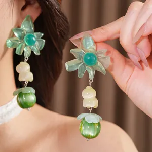 Dettaglio di orecchini in resina esagerati con fiori verdi e un ciondolo a forma di pony.