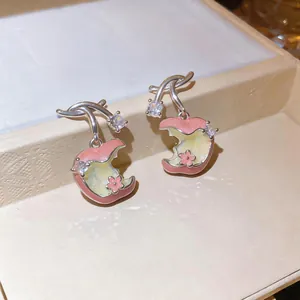 Detalle de pendientes de esmalte con forma de manzana, circonitas y flor rosa