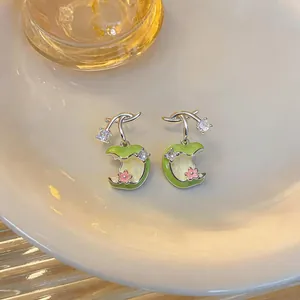 Primer plano de pendientes de manzana en esmalte con circonitas y flores rosadas.