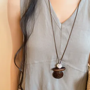 Detail view of retro ethnic long necklace with dark brown resin pendant on grey linen