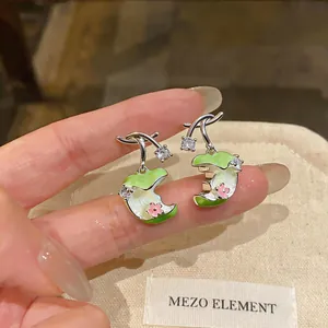 Detalle de pendientes de aguja de plata con circonitas y diseño de manzana verde