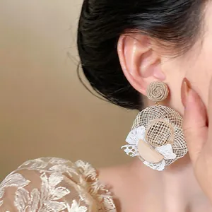 Close-up detail of woven straw hat earring with white lace trim and wooden crescent accent