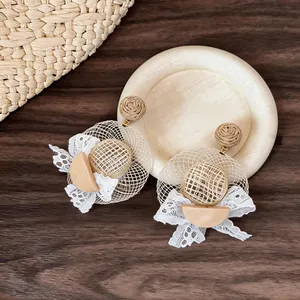 Detailed macro view of handcrafted woven straw hat earrings with elegant white lace bows.