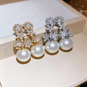 Close-up of elegant zircon flower earrings with large pearls in gold and silver tones.
