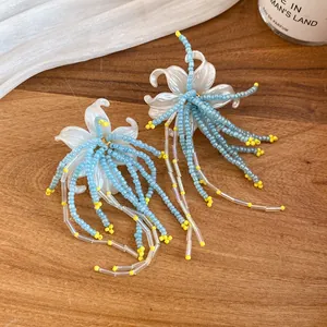 Detailed view of white floral earrings with blue beaded tassels on a wood surface
