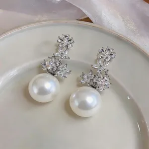 Detailed close-up of elegant zircon flower and large pearl drop earrings on a ceramic tray