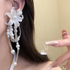 Detailed view of elegant white flower tassel earrings with pearls on a model's ear