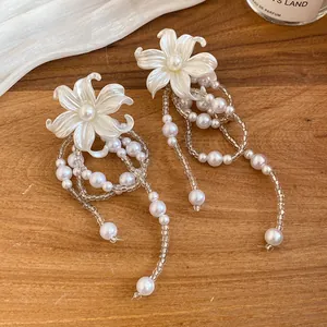 Close-up of white flower earrings with cascading pearl and bead tassels on wood.