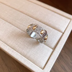 Primer plano de un anillo abierto grabado con óvalos dorados y banda plateada