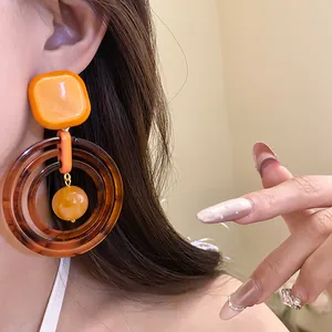 Close-up of vintage Maillard style resin dangle earrings in orange and brown.