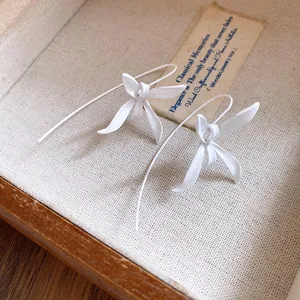 Close-up of elegant white matte flower drop earrings displayed in a vintage wooden box
