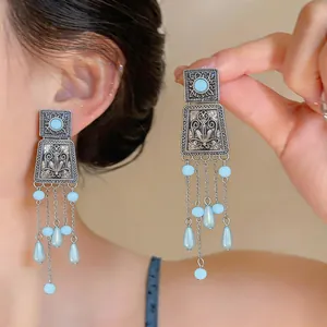 Detailed view of vintage square engraved stud earrings with light blue beads and long tassels.