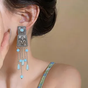 Close-up of bohemian tassel earrings with blue beads and silver embossed pattern.