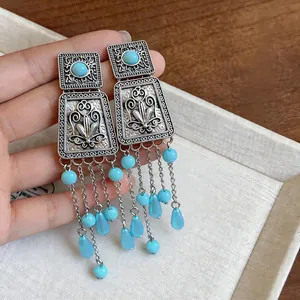 Detailed view of ethnic square earrings with turquoise beads and metallic tassels
