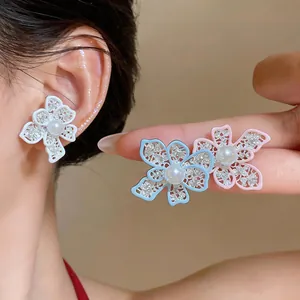 Close-up of elegant hollow floral pearl stud earrings in white, blue and pink