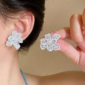 Detailed view of hollow white flower stud earrings with pearl center and silver needles