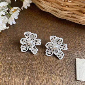 Macro view of white enamel hollow lace flower stud earrings with a central pearl