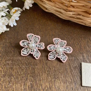 Close-up of pink enamel hollow flower earrings with intricate lace details and white pearls