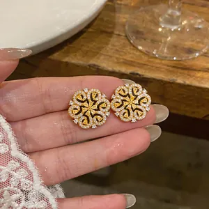Close-up of 18K gold-plated floral stud earrings with yellow zircons held by hand.