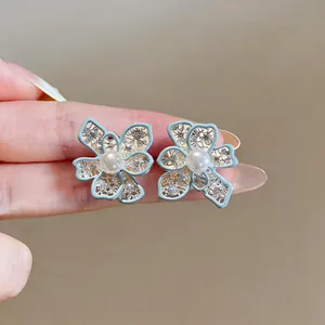 Close-up of light blue enamel hollow flower earrings with central pearl details.