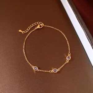 Elegante bracciale dorato con tre zirconi ovali viola su un supporto scuro testurizzato.