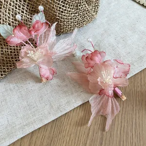 Close-up of two pink fabric flower hair clips with pearls on a linen background.