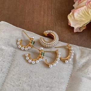 Dettaglio di orecchini placcati oro 18k con perle e zirconi su un cuscino decorativo