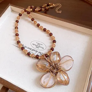 Dettaglio ravvicinato di una collana vintage con ciondolo fiore in vassoio di legno