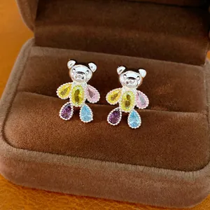 Macro view of silver bear stud earrings featuring colorful teardrop zircon stones on velvet.