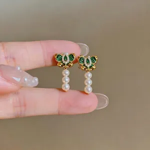 Primo piano di orecchini a farfalla vintage con smalto verde e perle.