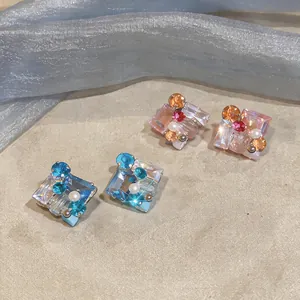Detalle de pendientes cuadrados con cristales de colores brillantes y perlas.